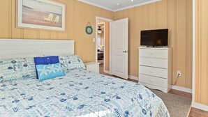 Une chambre à coucher comprenant un lit, une télévision, une commode et une porte donnant sur une autre pièce.