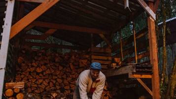 Una persona cortando madera dentro de un rústico cobertizo de madera rodeado de un bosque.