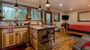 Interior acogedor de una cabaña con cocina de madera, comedor, cama y televisor.
