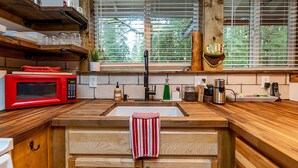 Una cocina con encimeras de madera, un microondas rojo, un fregadero y una ventana con persianas.