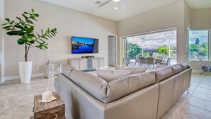 A spacious living room with a large beige sofa, a flat-screen TV, and a potted plant. - Full of Sunshine House, Modern, Waterfront w/ Beautiful Heated Pool (Cape Coral)