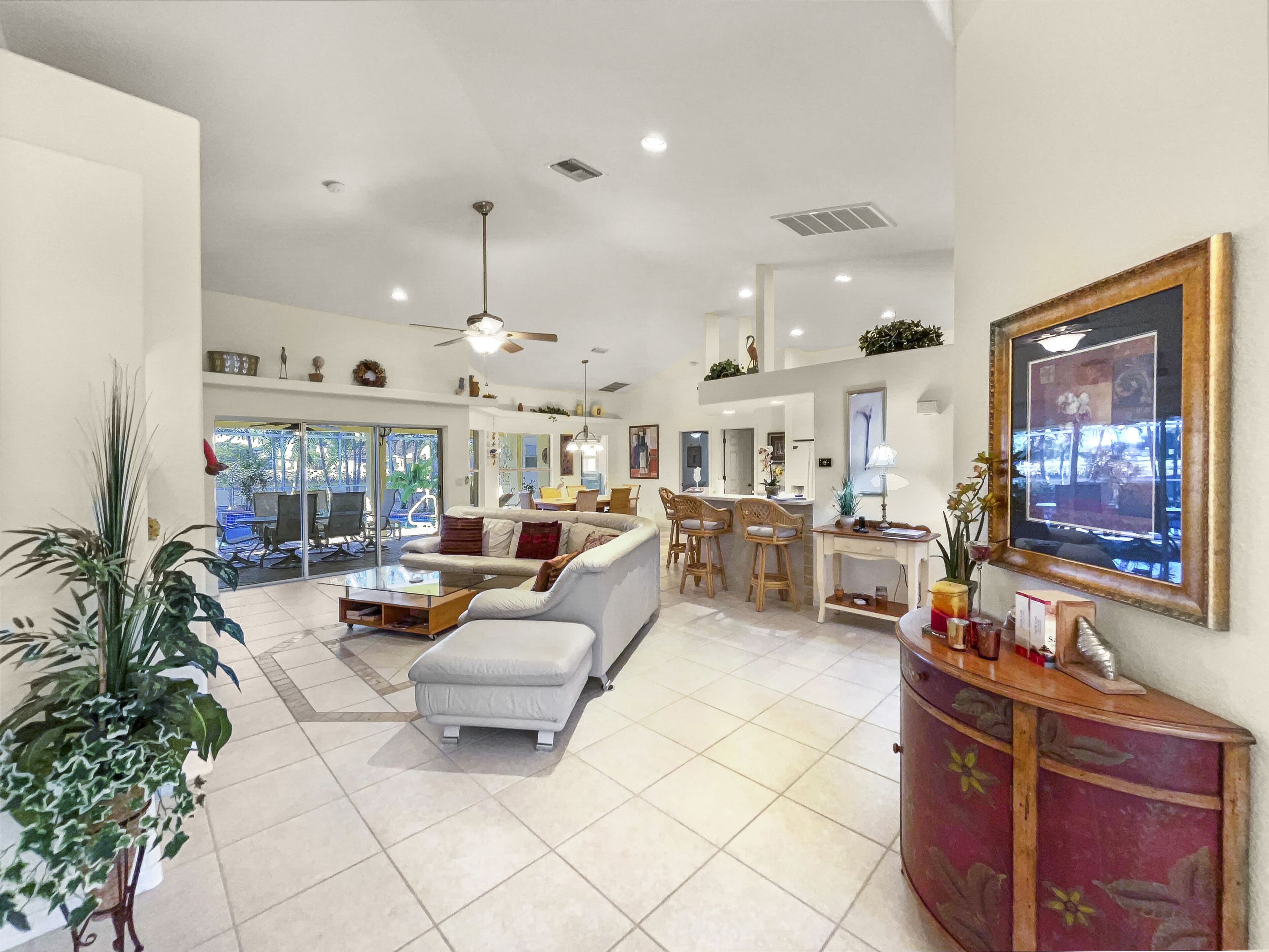 A spacious living area with a sofa, coffee table, and a dining area with chairs. There is a TV on the wall and a ceiling fan.