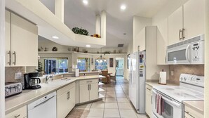 Una cocina moderna con armarios blancos, una isla central, horno empotrado y microondas.