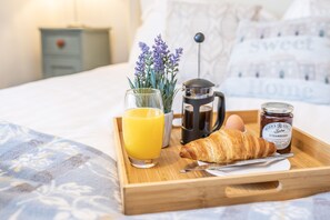 A breakfast tray with a croissant, a glass of orange juice, a coffee pot, a jar of strawberry jam, and a boiled egg on a bed. - Seaside Snug (Great Yarmouth)