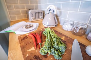 A kitchen counter with a cutting board, broccoli, red chili peppers, a knife, a toaster, and a kettle. - Seaside Snug (Great Yarmouth)