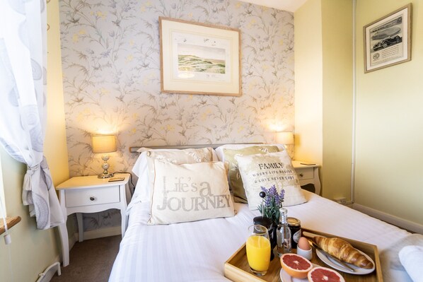 A neatly made bed with pillows, a bedside table with a lamp, a tray with breakfast items, and a framed picture on the wall.