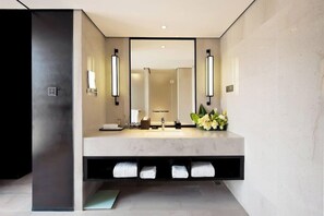 A modern bathroom with a large mirror, two wall-mounted lights, a marble sink, and a towel rack with towels.