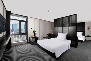 A modern hotel room with a large bed, a desk, a chair, a TV, and a view of the city.