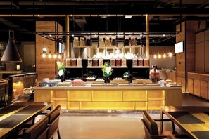 A restaurant interior with a central bar, wooden walls, hanging pendant lights, and a variety of food items displayed on shelves.