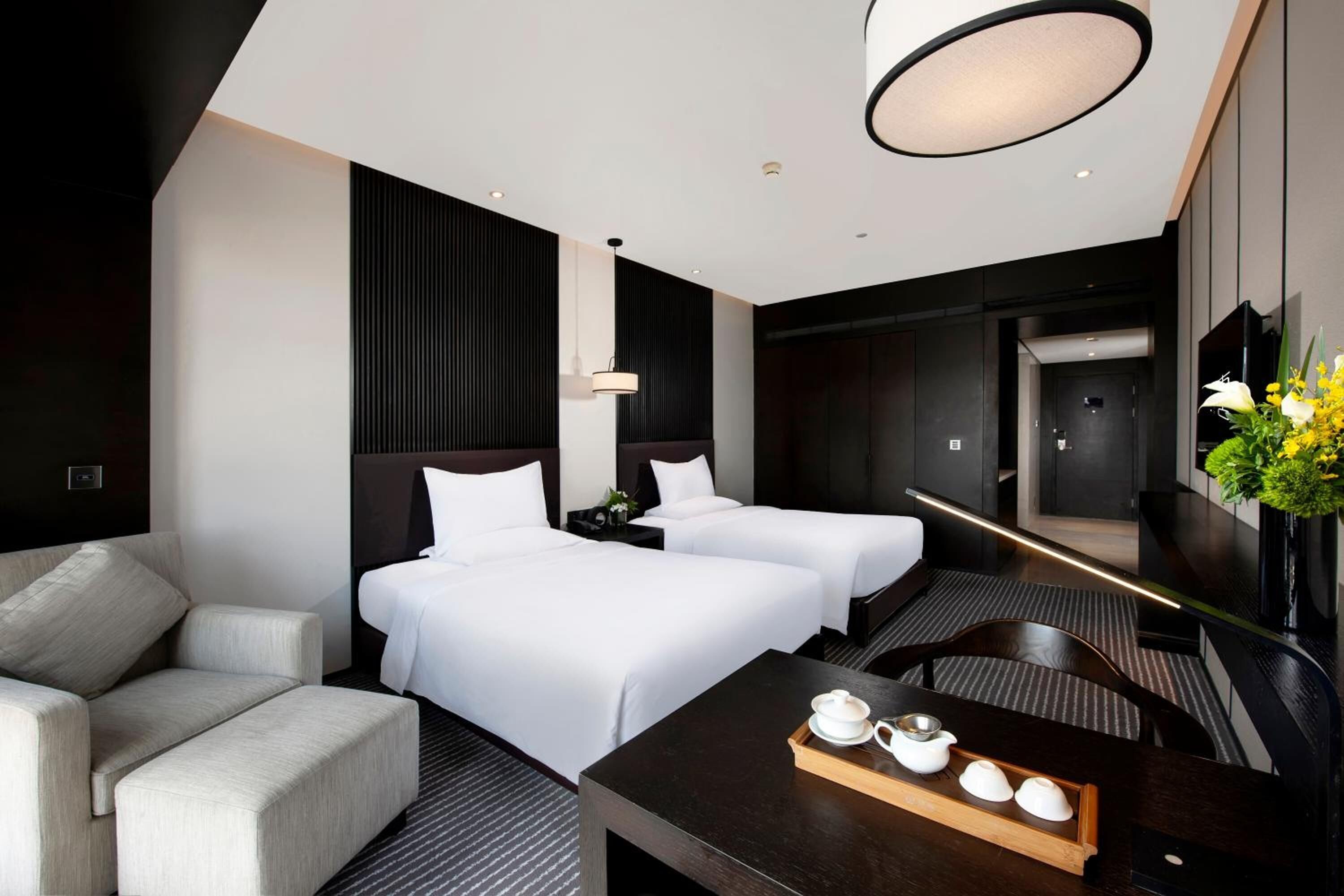 A modern hotel room with two beds, a sofa, a dining table with tea set, and a large mirror.