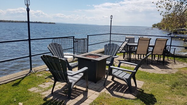 Un espace extérieur aménagé avec des chaises Adirondack et une table carrée, offrant une vue sur une étendue d’eau.