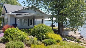 Une maison dotée d’un porche abrité, offrant une vue sur un lac, et agrémentée de diverses plantes et arbustes au premier plan.