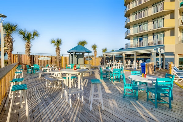 Relax on the deck with comfortable seating and shade from umbrellas, surrounded by lush palm trees and a scenic view.