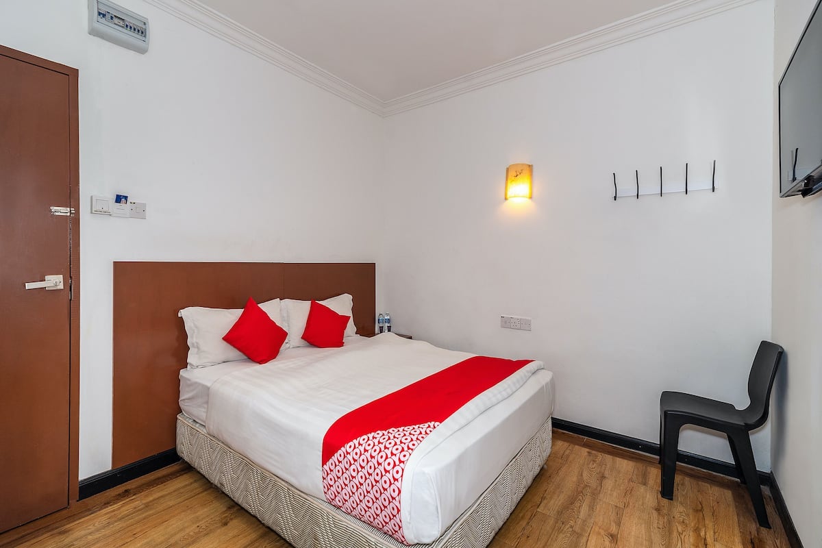 A hotel room with a bed, a chair, a wall-mounted light, and a door.