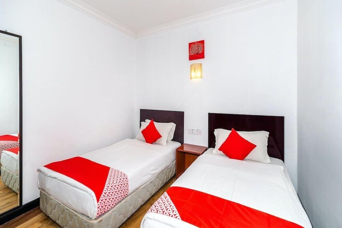 A hotel room with two single beds, each with a red and white bedspread and pillows.