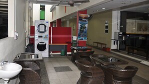 A public laundry area with a washing machine and dryer, wicker furniture, a sink, and a glass partition. - Super OYO 89847 Switz Paradise Hotel (Kota Kinabalu)