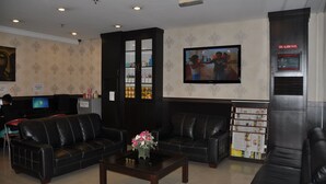 A lobby with two black leather sofas, a coffee table with flowers, a television, and a fire alarm panel. - Super OYO 89847 Switz Paradise Hotel (Kota Kinabalu)
