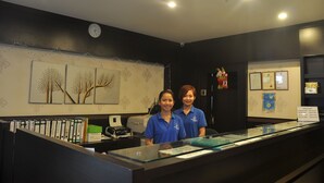 A reception desk with two staff members, a clock, framed certificates, and a decorative tree painting. - Super OYO 89847 Switz Paradise Hotel (Kota Kinabalu)
