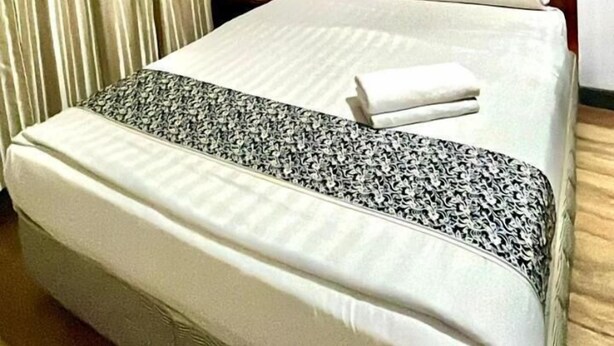 A hotel room with a bed, curtains, an air conditioning unit, a small table with a plant, and a wall-mounted air conditioning unit. - Super OYO 89847 Switz Paradise Hotel (Kota Kinabalu)