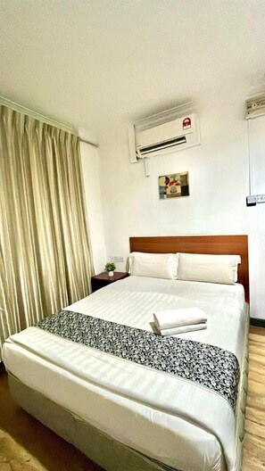 Ein Hotelzimmer mit Bett, Vorhängen, einer Klimaanlage, einem kleinen Tisch mit Pflanze und einer Wandklimaanlage.