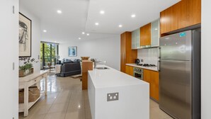 Eine moderne Küche mit Kochinsel, Holzschränken, einem Edelstahlkühlschrank und einer Essecke mit Sofa und Tisch.