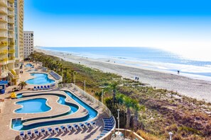 Un hotel con varias piscinas, una playa y vistas al océano.