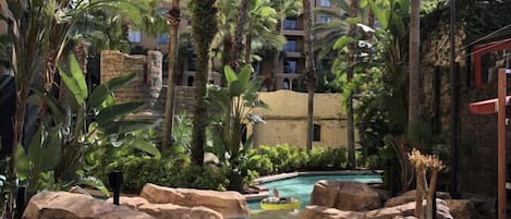 A resort pool area with natural rock formations, palm trees, and a clear blue pool.