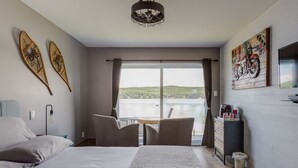 Une chambre à coucher avec un lit, une chaise, une table, une vue sur un lac et un tableau accroché au mur.