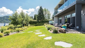 Un bâtiment moderne doté d’un balcon donnant sur un jardin bien entretenu et un lac.