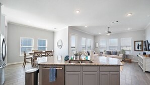 Una cocina amplia con una isla grande, un comedor con mesa y sillas, y una sala de estar con sofá y televisor.
