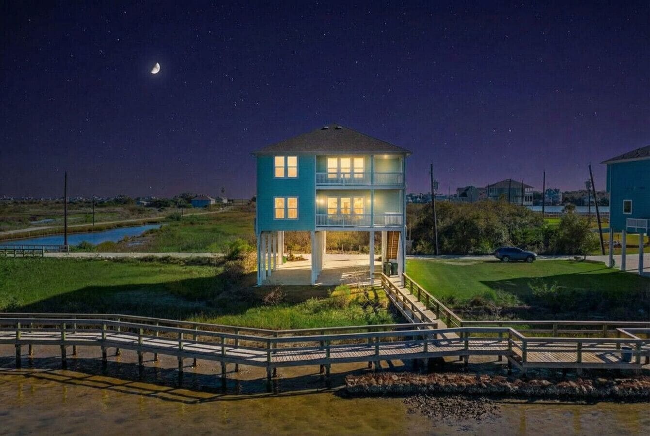 A two-story building with a balcony, situated near a body of water, with a wooden walkway leading to it.