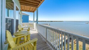 Una terraza de madera con sillas Adirondack amarillas que dan a una masa de agua tranquila.