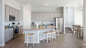 Una cocina moderna con armarios blancos, una isla central con taburetes, electrodomésticos de acero inoxidable y suelo de madera.