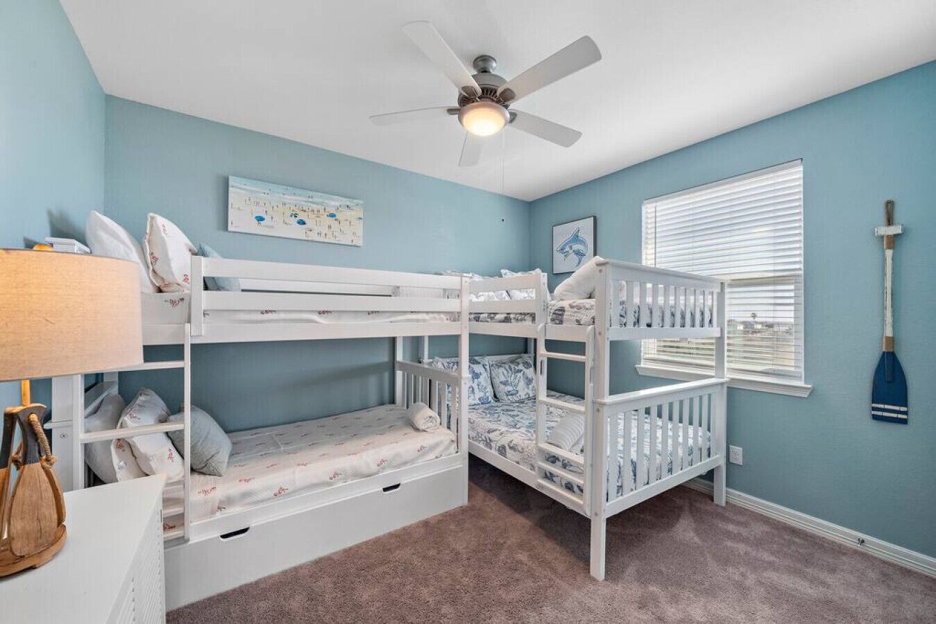 A child's room with bunk beds, a ceiling fan, a window with blinds, and a mop on the wall.