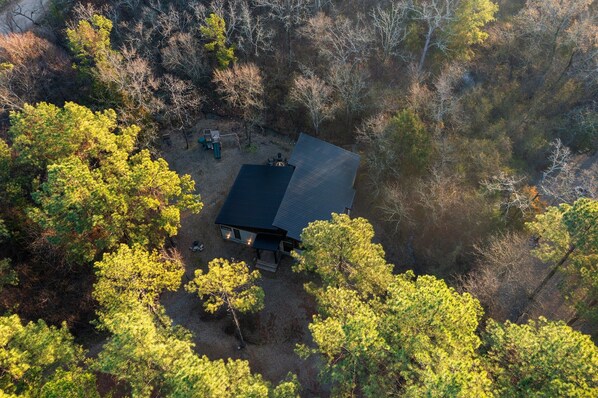 Une vue aérienne d’une cabane entourée d’une forêt dense, sous un ciel dégagé.