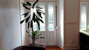 A room with a wooden floor, a large potted plant, a red chair, and a door leading to a balcony. - Green View Home (Lisbon)