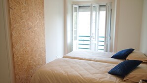 A bedroom with two beds, a wooden wall, and a window with blinds. - Green View Home (Lisbon)