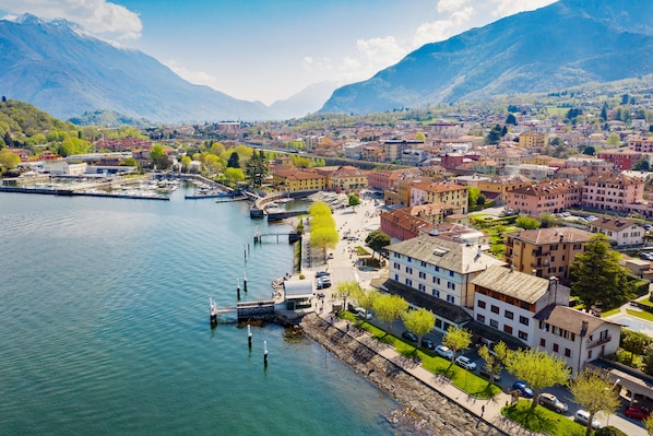 A lakeside town with buildings, a dock, and mountains in the background. - Margherita (Colico)