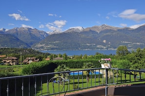 Un balcón con vistas a montañas, un lago y una piscina.