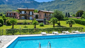 A pool with lounge chairs, a house with balconies, and a mountainous backdrop. - Iris (Colico)