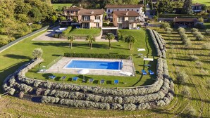 A large, rectangular swimming pool surrounded by a stone wall, with several lounge chairs and umbrellas. - Iris (Colico)