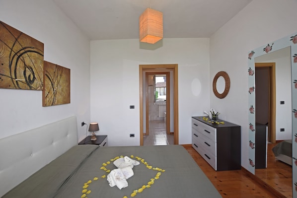 A bedroom with a bed, a dresser, a mirror, and artwork on the walls. - Iris (Colico)