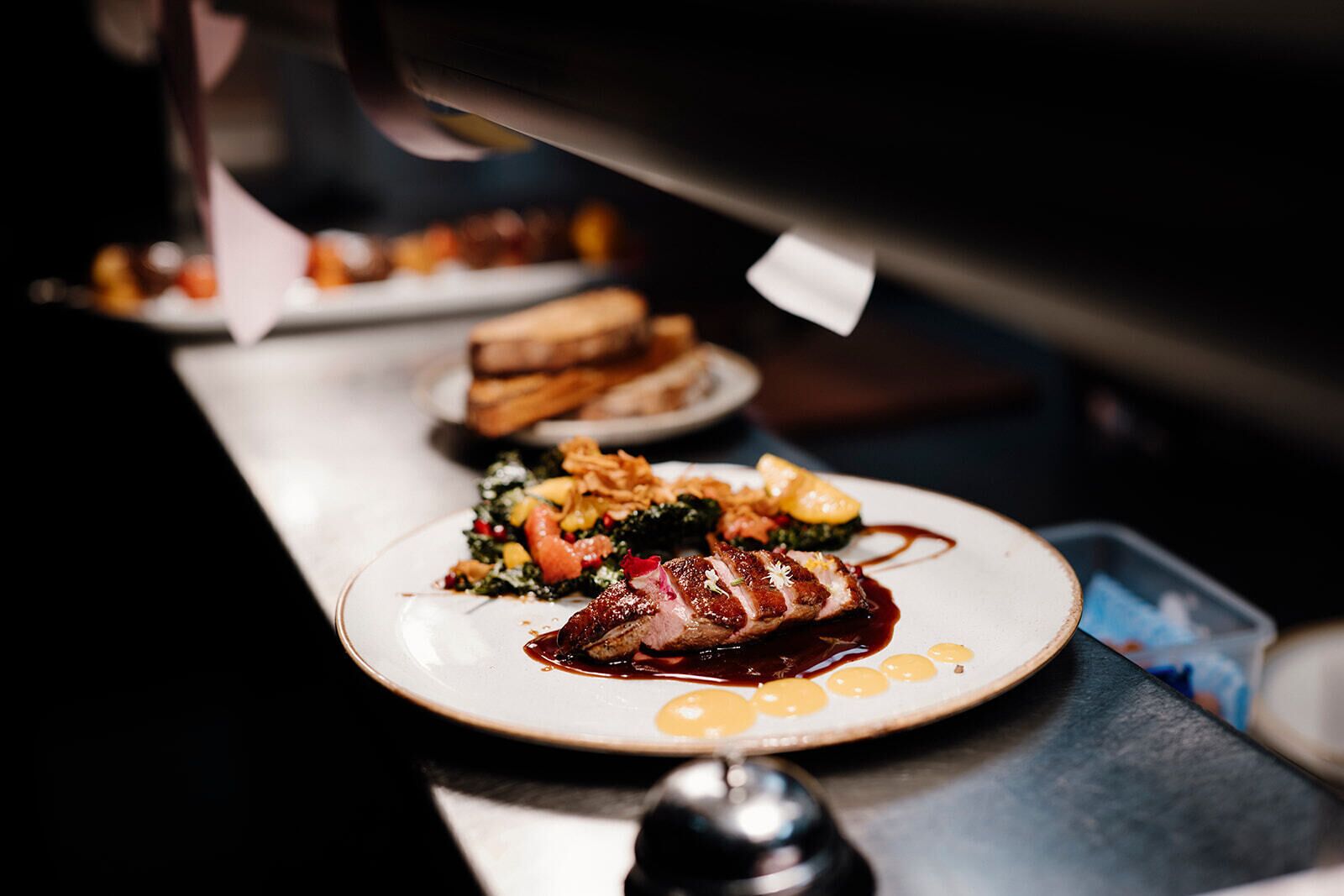 A restaurant setting with a focus on a plate of food, including a steak and vegetables, and a dessert with a sauce.