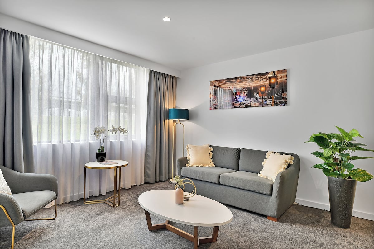 A modern living room with a grey sofa, a round coffee table, a floor lamp, and a large window with sheer curtains.