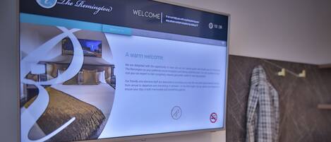 Pantalla de bienvenida digital del hotel The Remington, mostrando un interior moderno y un mostrador de recepción con un bolso de mano.