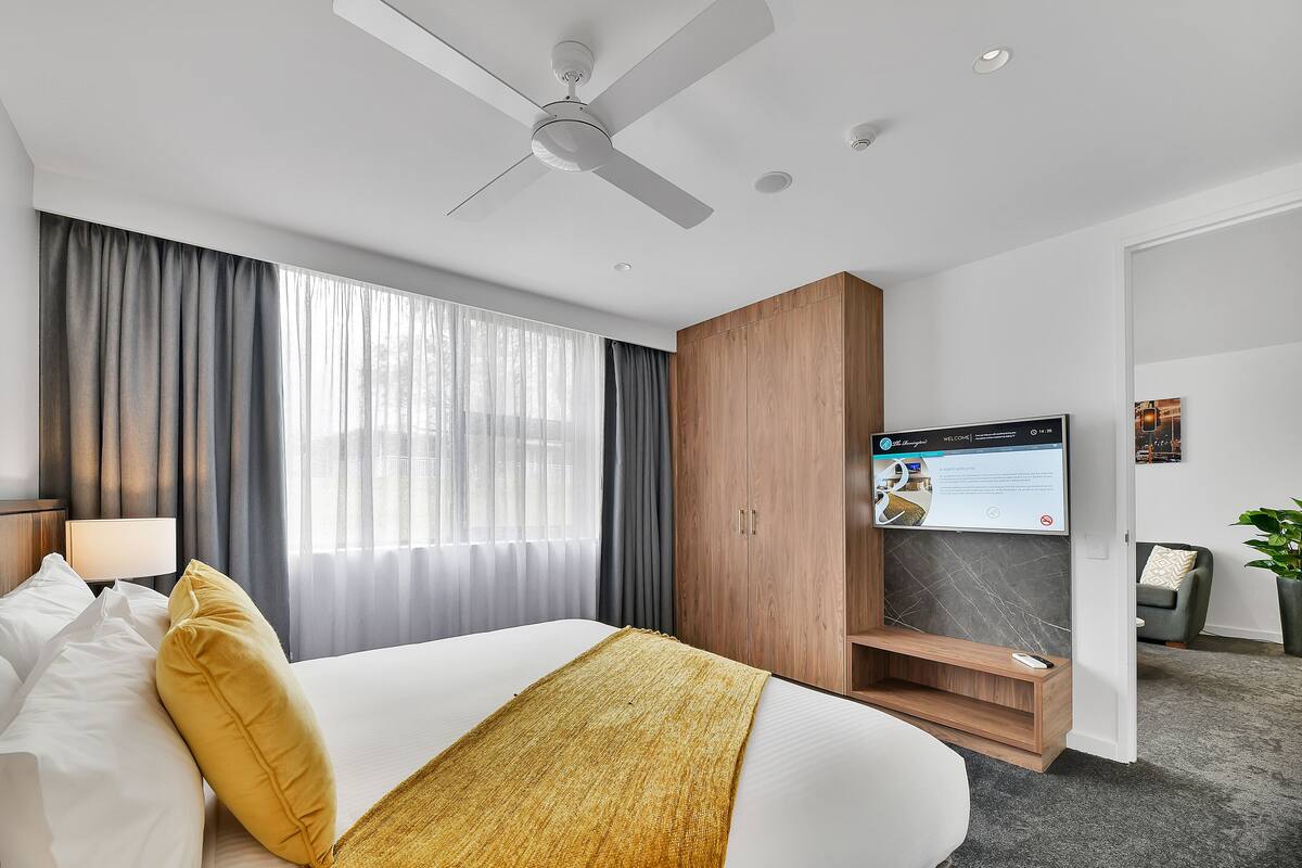 A modern hotel room with a bed, a television, a ceiling fan, and a desk area.