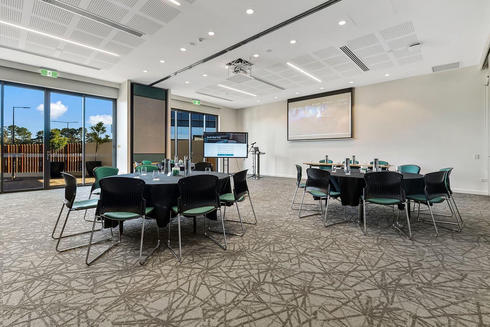 A conference room with a large screen, multiple tables, and chairs.