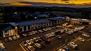 A large parking lot with multiple rows of parked cars and a building with a flat roof in the background. - The Remington Orange (Orange)
