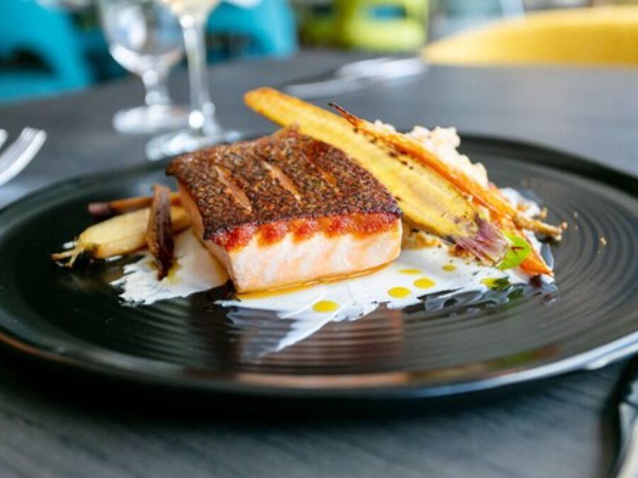 Un plato con un trozo de pescado, papas fritas y una ensalada pequeña.