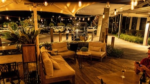 An outdoor seating area with sofas and tables, surrounded by plants and under string lights. - The Remington Orange (Orange)